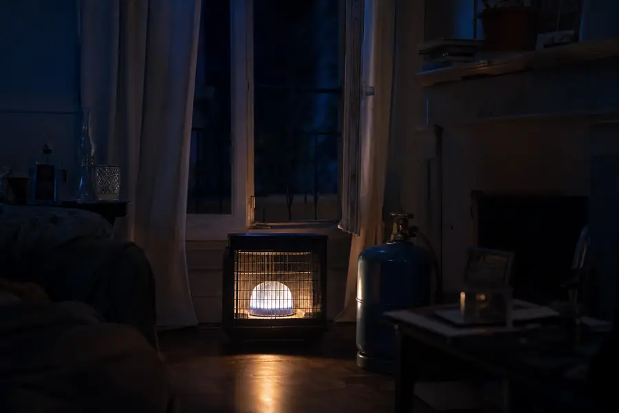 Radiateur à gaz d'appoint fonctionnant sur bouteille de butane dans un salon faiblement éclairé, avec fenêtre entrouverte
