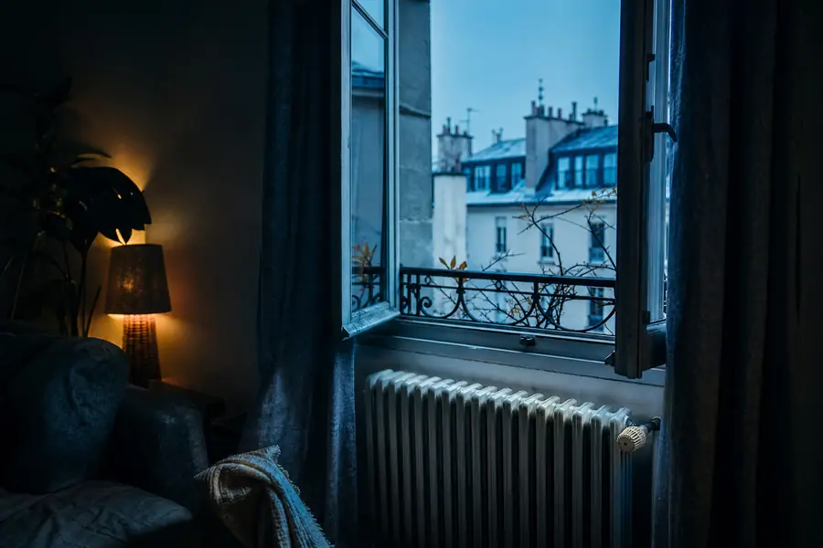 Fenêtre entrouverte dans un salon chauffé au gaz en hiver, avec un radiateur visible au premier plan.